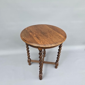 May include: A round wooden side table featuring a dark brown finish with a visible wood grain pattern. The table is supported by four legs, each designed with a twisted barley sugar style, connected by a central cross-shaped stretcher base.