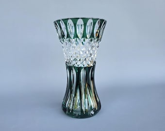 Puede incluir: Un jarrón de cristal verde y transparente con una parte superior acampanada y un patrón tallado en diamante. La base es de color verde oscuro, que se desvanece a cristal transparente en el medio, y un borde verde.