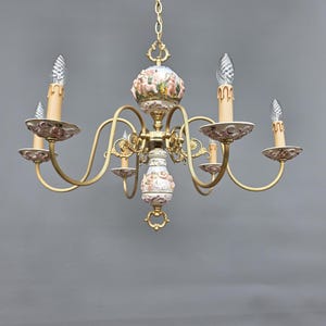 May include: A vintage chandelier with a gold-toned frame and five curved arms. The chandelier features decorative porcelain elements with floral and cherub designs. Each arm holds a candle-shaped light fixture with a clear, textured bulb.