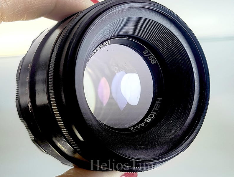 Puede incluir: Un objetivo de c&aacute;mara negro Helios-44-2 con una distancia focal de 58 mm y una apertura de f/2. El objetivo tiene un anillo de enfoque estriado y marcas de apertura. Dise&ntilde;ado para su uso con una c&aacute;mara, tiene un elemento de vidrio transparente.
