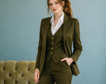 May include: A three-piece olive green suit with a white collared shirt. The suit includes a blazer, vest, and trousers. The blazer has two buttons, and the vest has four gold buttons. The person is standing in front of a light blue wall.