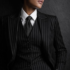 Puede incluir: Un traje de raya diplom&aacute;tica negro con camisa blanca y corbata estampada. El traje incluye blazer, chaleco y pantal&oacute;n. El modelo lleva camisa blanca y corbata estampada.