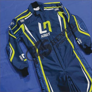 Könnte beinhalten: Marineblauer Kart-Rennanzug mit weißen und neongelben Akzenten. Der Anzug zeigt das Wort "KART" in weißen Buchstaben und die Marke "OMP". Die Ärmel und Beine haben zusätzliche Text- und Designelemente.