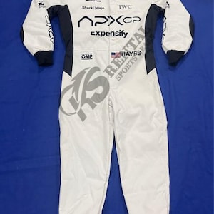 Puede incluir: Mono de carreras blanco con detalles en negro, con logotipos de patrocinadores como "OMP", "IWC" y "Expensify". El mono tiene un parche de la bandera estadounidense y el texto "HAYES SPORTS".