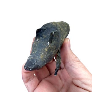 Peut inclure: Petite sculpture artisanale d'un hippopotame. L'hippopotame est peint en noir avec des reflets dorés et des yeux blancs. La sculpture est tenue dans une main sur fond blanc.