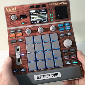 Könnte beinhalten: Ein Akai MPC Sample Musikproduktionsgerät mit Holzmaserung. Es verfügt über zahlreiche Knöpfe, Pads und einen Bildschirm, der Audio-Wellenformen anzeigt. Das Gerät wird von Händen gehalten und trägt den Text "Lofiandy.com".