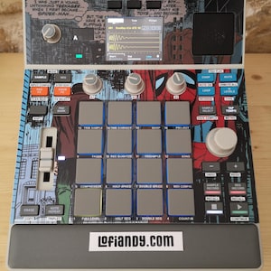 May include: A digital music production device with a Spider-Man comic book design. It features numerous buttons, knobs, and a screen displaying audio waveforms. The device has the text "Lofiandy.com" on the front.