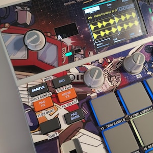May include: A digital music production device with a cartoon design. It features buttons labelled "Sample", "Flex Beat", and "Pad Bank". A screen displays audio waveforms. Knobs and pads are visible. Measurements are not applicable.