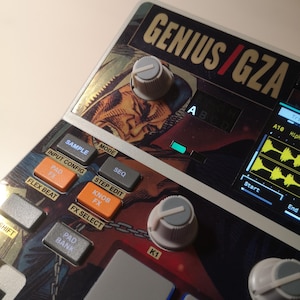 May include: A close-up shot of a black and grey electronic music production device. The device has the text "GENIUS/GZA" and buttons labelled "SAMPLE", "MODE", "PAD FX", and "KNOB FX". It features knobs and a small screen displaying a waveform.