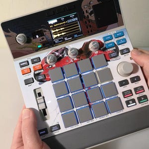 May include: A custom-designed music production device featuring a colorful graphic overlay. The device has numerous buttons, pads, and knobs, with a screen displaying audio waveforms. The design includes anime-style artwork and a red car graphic.