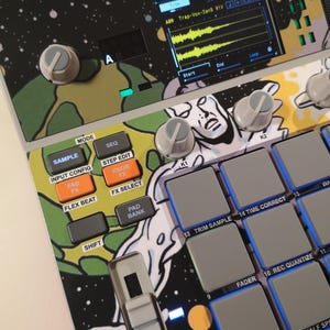 May include: A music production sampler featuring a colourful space-themed graphic overlay. The device includes a digital screen displaying audio waveforms, multiple grey rubber pads, control knobs, and buttons labelled with functions like Sample, Seq, and Pad Bank.