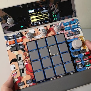 Puede incluir: Un dispositivo de producción musical digital con un diseño gráfico colorido de Dragon Ball Z. El dispositivo presenta numerosos botones, perillas y una pantalla que muestra formas de onda de audio. El diseño incorpora imágenes de personajes de la serie de anime.