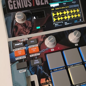 May include: A close-up of a music production device with the text "GENIUS / GZA". The device features buttons, knobs, and a screen showing audio waveforms. The design incorporates comic book style artwork. The device has a black and white color scheme.