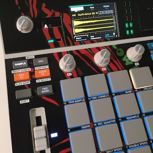 May include: A black and white electronic music production device with a screen displaying audio waveforms. It features numerous buttons, knobs, and pads, with orange and blue illuminated controls. The device has a red and black patterned design.