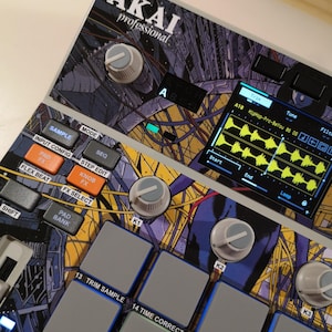 May include: An Akai Professional music production controller featuring a colourful graphic skin with purple, yellow, and blue abstract patterns. The device includes a digital screen displaying audio waveforms, multiple grey square pads, and white knobs.