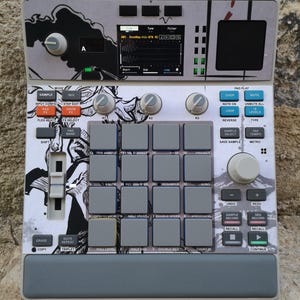 May include: A grey and white music production device with multiple buttons, knobs, and pads. The device has a small screen showing waveforms and text. The top panel features a black and white graphic design. Designed for music production and beat making.
