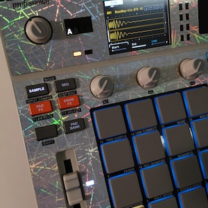 May include: A close-up of an Akai MPC SP sampler. The device has a silver and gray finish with numerous buttons, knobs, and a screen displaying audio waveforms. The text "AKAI professional" is visible on the top left.