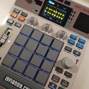 May include: An Akai Professional MPC Sampler featuring a light grey chassis, a central digital display showing waveform data, sixteen square grey pads with blue borders, various control knobs, and buttons labelled with functions like Chop, Mute, and Tap Tempo. The text lofianpy.com is printed on the lower left corner.
