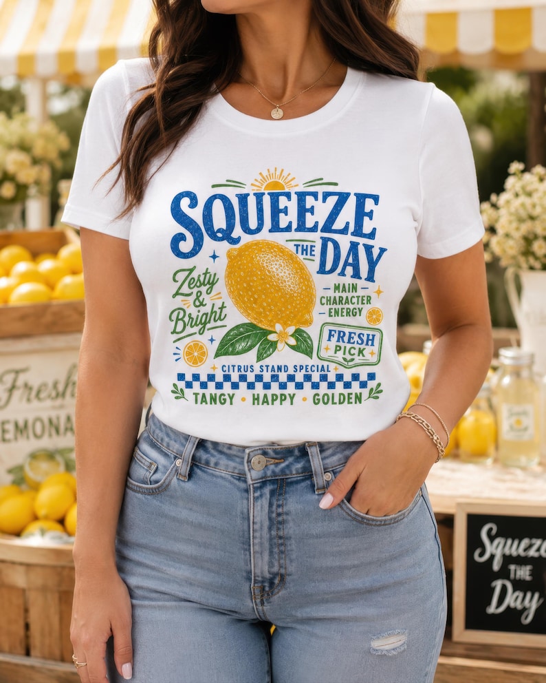 May include: A white short-sleeve t-shirt featuring a graphic print of a yellow lemon with green leaves and the text SQUEEZE THE DAY, Zesty & Bright, Main Character Energy, Fresh Pick, Citrus Stand Special, Tangy, Happy, Golden in blue and green.