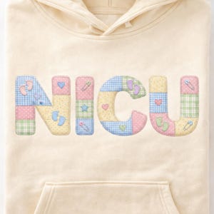 Puede incluir: Sudadera con capucha color crema con la palabra "NICU" en la parte delantera. Las letras son de estilo patchwork, con cuadrados rosas, azules y amarillos pastel. Cada letra está decorada con pies de bebé, corazones, estrellas y imperdibles.
