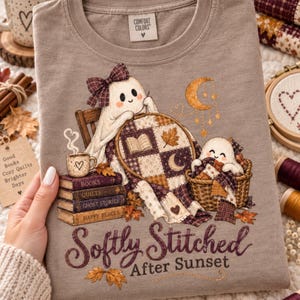 May include: A taupe t-shirt featuring a graphic of two ghosts crafting with a quilt, a stack of books labeled Books, Quilts, Ghost Stories, and Happy Places, and the text Softly Stitched After Sunset. The design includes a crescent moon and stars.