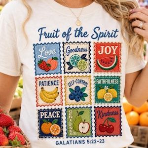 Op de afbeelding: Crèmekleurig T-shirt met een kleurrijke afbeelding van vierkante postzegels. Elke vierkant toont een vrucht en een woord: Liefde, Goedheid, Vreugde, Geduld, Zelfbeheersing, Trouw, Vrede, Zachtmoedigheid en Vriendelijkheid. De tekst "Vrucht van de Geest" en "Galaten 5:22-23" zijn ook aanwezig.