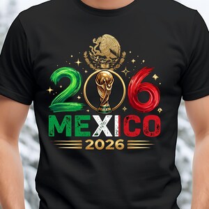 May include: A black t-shirt featuring a graphic with the number 206, where the zero is replaced by a gold FIFA World Cup trophy. Above is the Mexican coat of arms. Below, the word MEXICO is in green, white, and red, followed by 2026 in gold.
