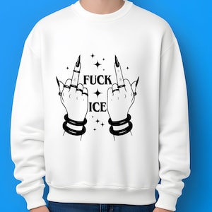 May include: White sweatshirt featuring a black graphic of two hands displaying the middle finger, accompanied by the text "FUCK ICE" and star motifs. The hands have long, black nails and are accessorized with rings and bracelets. A striking design.
