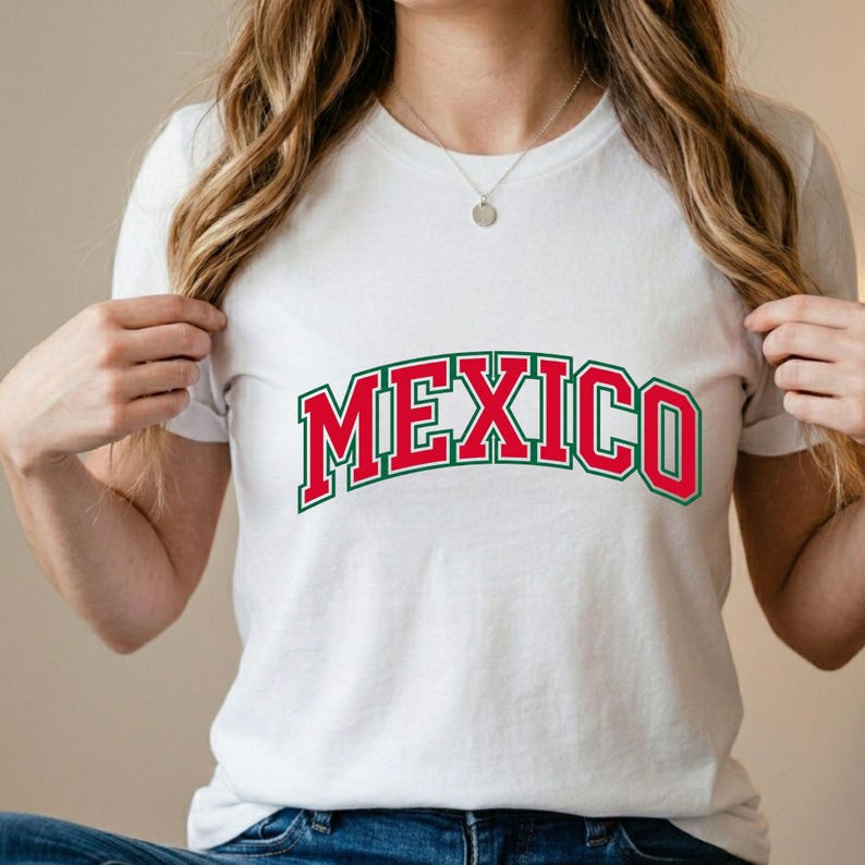 May include: A white short-sleeved t-shirt featuring the word MEXICO printed in a bold, arched collegiate font. The lettering is red with a dark green outline. The shirt has a classic crew neckline and is made of a plain, solid white fabric.