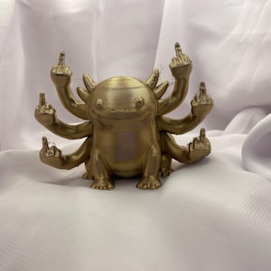 Peut inclure: Une figurine de couleur or métallique représentant une créature avec une tête arrondie, des branchies externes et six bras. Chacun des six bras est étendu vers l'extérieur, chaque main faisant un geste de doigt d'honneur.