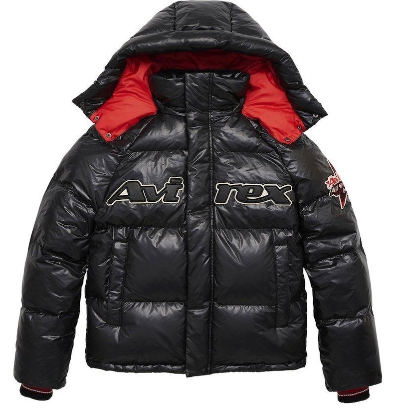 May include: Black puffer jacket with a hood and red lining. The jacket features the text "Avirex" in white and black, along with a small patch on the sleeve. The jacket has a shiny, quilted appearance.