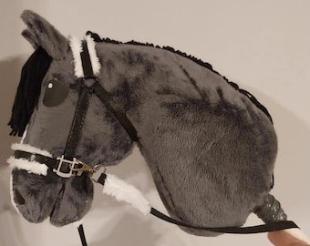 May include: A plush gray hobby horse with a black mane and bridle. The horse features white accents on the face and bridle, and a black rein. The toy is designed to be held and ridden, offering a playful experience for children.