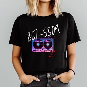 May include: Black t-shirt featuring a retro cassette tape design with the text "Retro Vibes" and the phone number 867-5309 in white script. The cassette tape design has purple, blue, and pink hues.