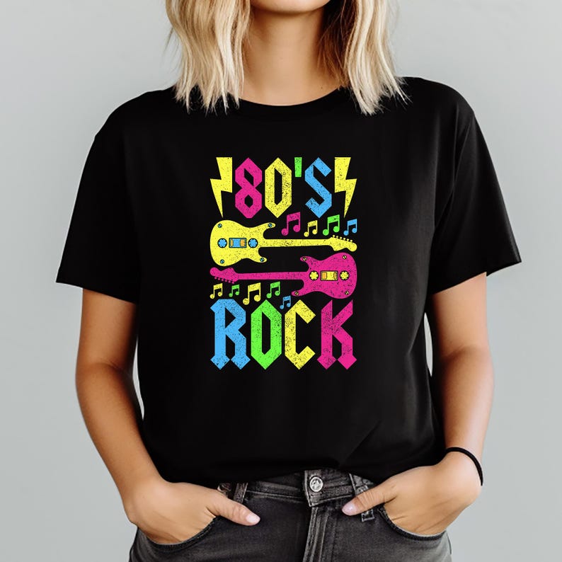 May include: Black t-shirt with a colorful graphic design. The design features the text "80's Rock" with a lightning bolt and two electric guitars in yellow, pink, and blue. Musical notes are also included in the design.
