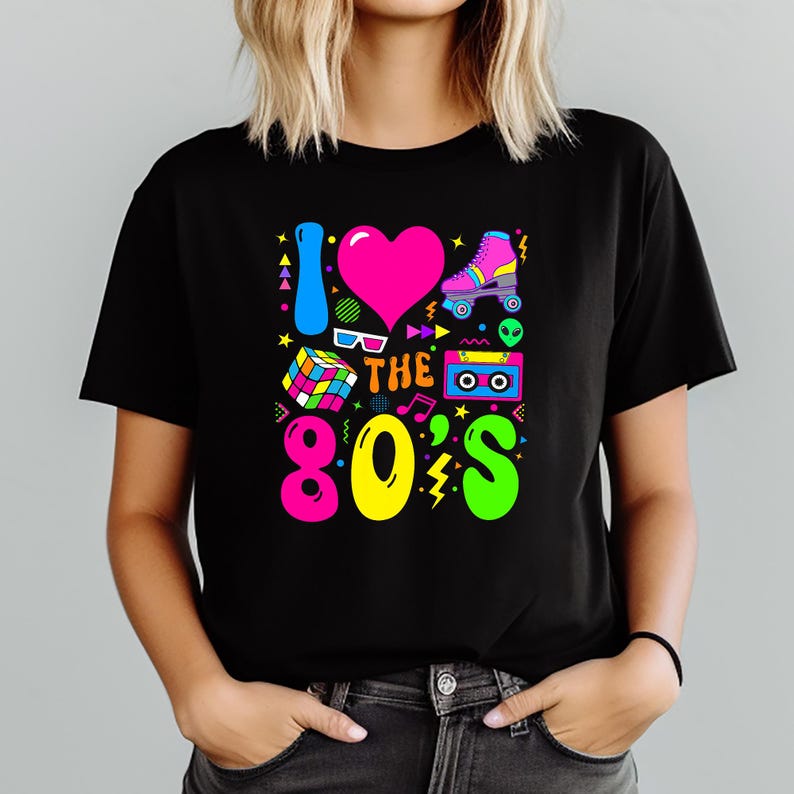 May include: Black t-shirt with a colorful graphic design. The design includes the text "I LOVE THE 80'S" with a pink heart, roller skate, Rubik's cube, cassette tape, and other 80s-themed icons in bright colors.