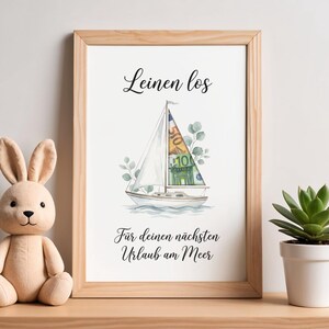 Può includere: Stampa incorniciata con un'illustrazione di una barca a vela con una vela fatta di banconote in euro. Il testo in tedesco "Leinen los" e "Für deinen nächsten Urlaub am Meer" è incluso. La cornice è marrone chiaro.