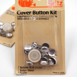 Op de afbeelding: Twee Ritz-sets voor het bekleden van knopen in beige kartonnen verpakking met doorzichtige plastic blisters. Elke set bevat zilverkleurige aluminium knopdoppen, witte plastic achterkanten, een knopenmaker en een duwer. Tekst 13 mm.
