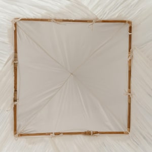 May include: A square, white paper parasol with a bamboo frame. The frame is a light brown color and is tied together with white string. The paper is a translucent white and is stretched tightly over the frame.