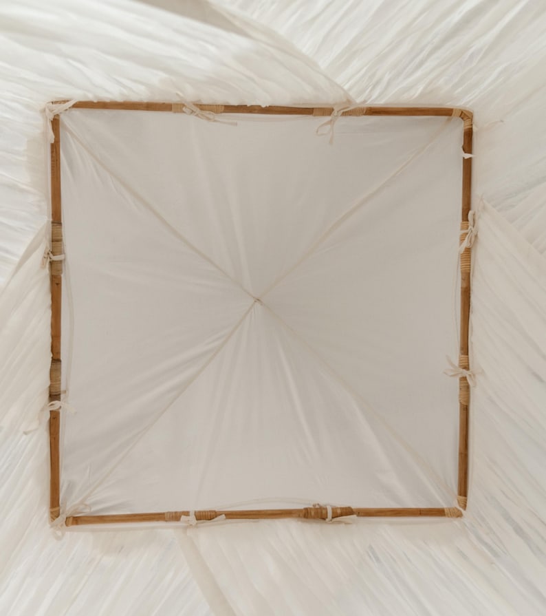 May include: A square, white paper parasol with a bamboo frame. The frame is a light brown color and is tied together with white string. The paper is a translucent white and is stretched tightly over the frame.