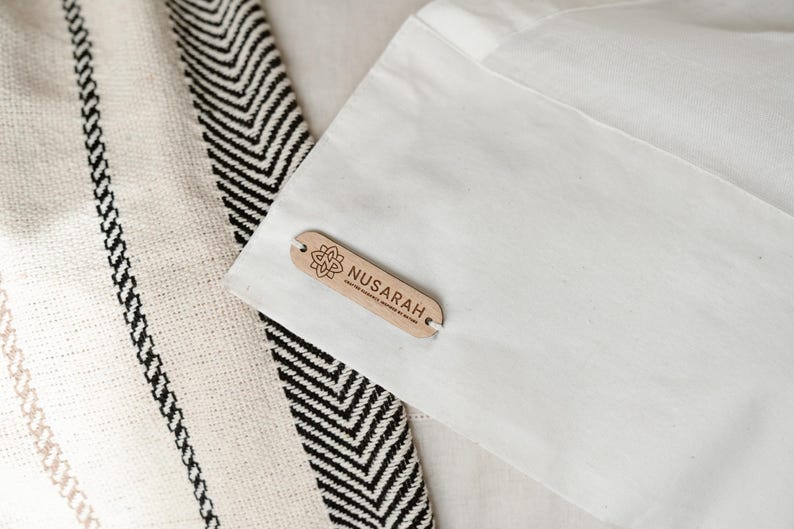 May include: Close-up of a textile with a black and white chevron pattern and a cream-colored fabric with black vertical stripes. A white fabric is in the background with a wooden tag that reads "NUSARAH".