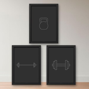 Puede incluir: Tres impresiones enmarcadas en negro con dibujos lineales blancos de equipos de fitness. La impresión superior presenta una pesa rusa, mientras que las dos inferiores muestran una barra y una mancuerna. Los marcos son rectangulares.