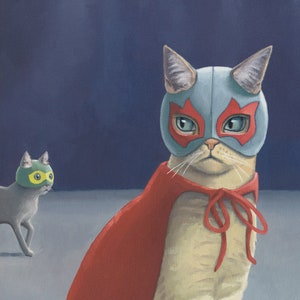 May include: A white cat wearing a red cape and a blue mask with red accents. The cat is sitting on a gray surface. A smaller gray cat with a green mask is in the background.