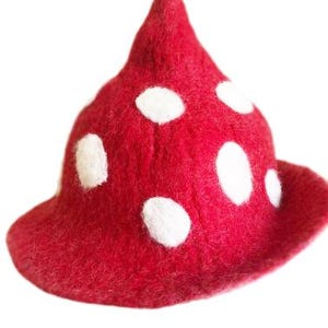 May include: A pointed hat made of red felted material featuring a pattern of circular white spots distributed across the surface. The hat has a conical crown and a slightly flared brim, resembling the appearance of a mushroom cap.
