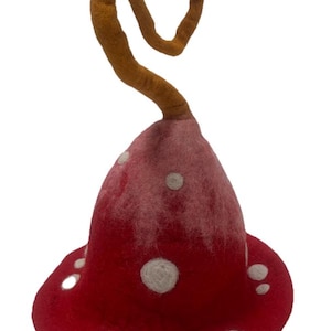 May include: A red felted hat with a bell-shaped crown and a wide brim. The surface features scattered white circular spots and a long, spiraling brown stem-like extension protruding from the top centre of the crown, crafted from felted wool.
