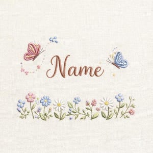 Puede incluir: Diseño bordado con la palabra "Name" en fuente marrón, con una mariposa rosa y otra azul. Un borde de flores bordadas en rosa, azul y blanco adorna la parte inferior. El fondo es de tela color crema.