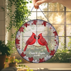 Könnte beinhalten: Runde Glasdekoration mit schwarzer Kette zum Aufhängen. Sie zeigt zwei rote Kardinäle auf einem Ast, mit dem Text "40. Hochzeitstag", Namen und einem Datum. Rote und silberne Blätter umrahmen das Bild.