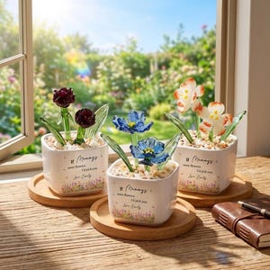 May include: Three decorative flower arrangements in white square pots on wooden coasters. Each pot has a different colored glass flower, including red roses, blue tulips, and orange and white flowers. The pots have the text "If Mummys were flowers I'd pick you Love Emily".