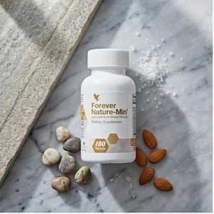 Op de afbeelding: Een witte fles "Forever Nature-Min" voedingssupplement met een schroefdop. De fles is omgeven door kleine stenen, amandelen en zoutkristallen. Het etiket geeft 180 tabletten aan.