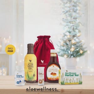 Puede incluir: Colección de productos Forever Living, incluyendo Aloe Vera Gel, Miel de Abejas, suplementos Arctic Sea y Té Herbal Aloe Blossom. También se incluye una bolsa roja con cordón y Active Pro-B. Los productos están sobre una superficie de madera.