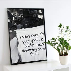 May include: Black and white framed print featuring a crowd of people. The central focus is a white t-shirt held up with the text: "Losing sleep for your goals is better than dreaming about them."